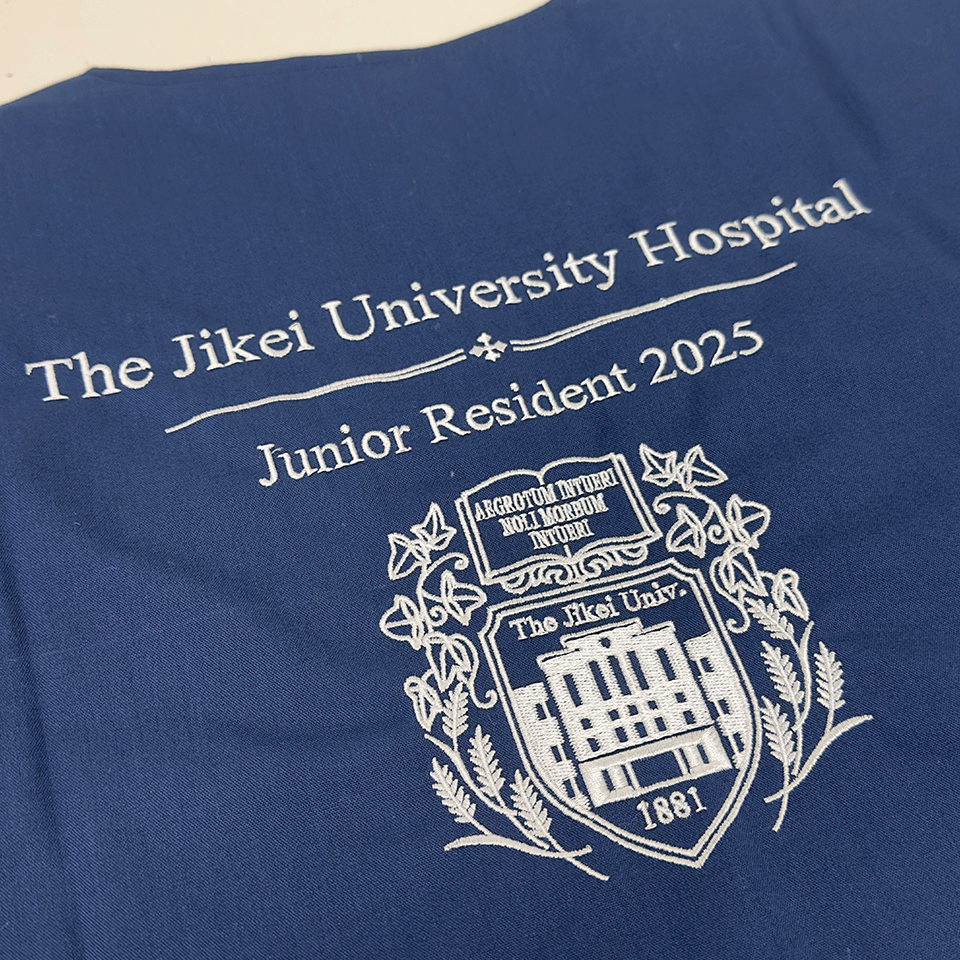 紺地のスクラブに施された、東京慈恵会医科大学附属病院の2025年研修医記念ロゴ刺繍
