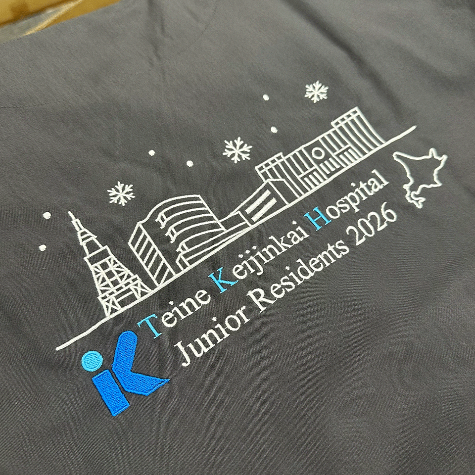 手稲渓仁会病院 研修医2026 スクラブ背中刺繍のアップ。札幌の街並みと病院ロゴ、北海道のシルエットが精緻な刺繍で表現されている。