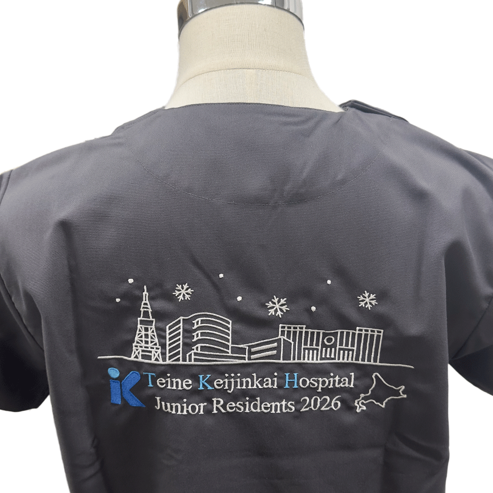 手稲渓仁会病院 研修医2026 スクラブ背中刺繍のアップ。札幌の街並みと病院ロゴ、北海道のシルエットが精緻な刺繍で表現されている。