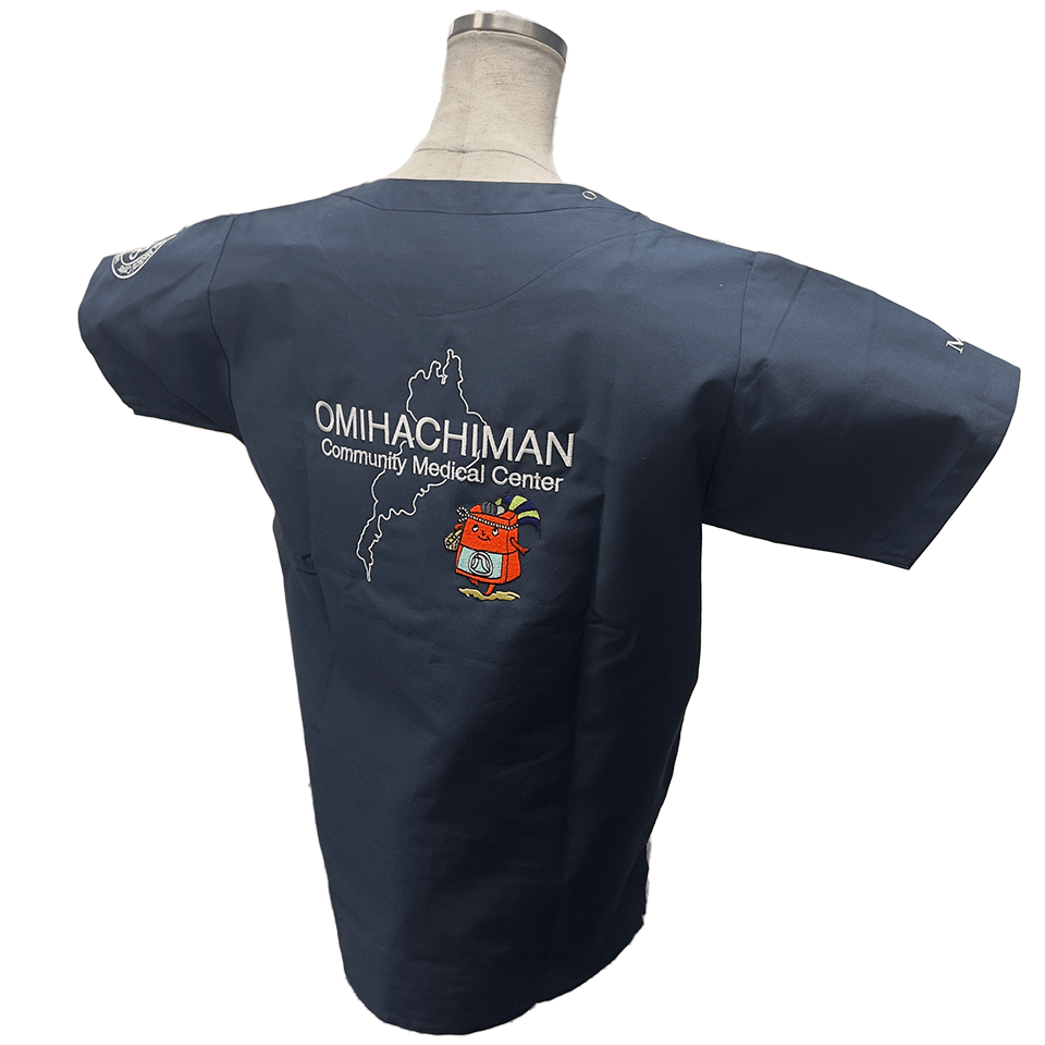 スクラブ背面の刺繍正面アップ。白の線地図で描かれた琵琶湖を背景に、「OMIHACHIMAN Community Medical Center」の文字と赤コン君が刺繍されている。