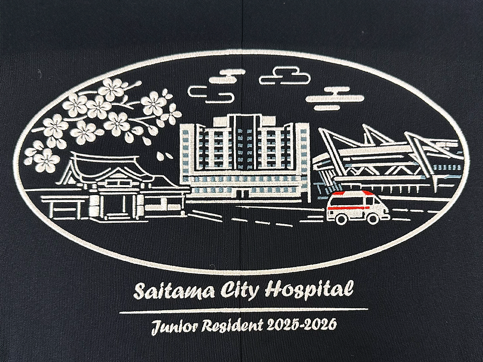 紺色のブルゾン背面に施された、さいたま市立病院「初期研修医 2025-2026」記念刺繍の全体像。さいたま市の街並みが楕円の中にデザインされている。